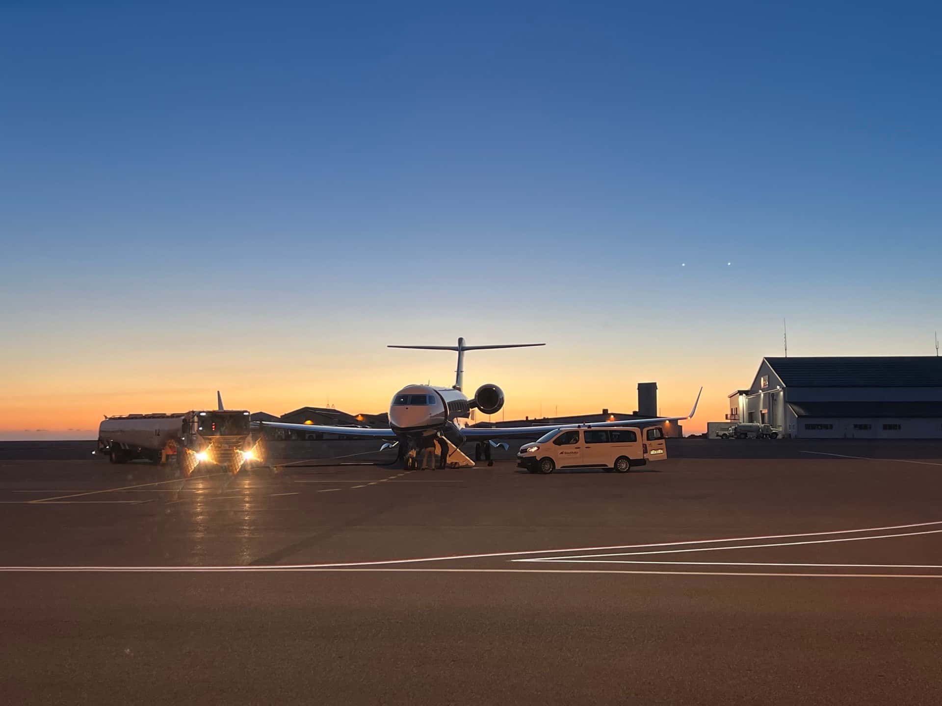 Private jet on the apron at Keflavík Airport at dusk with a One Luxury transfer vehicle waiting