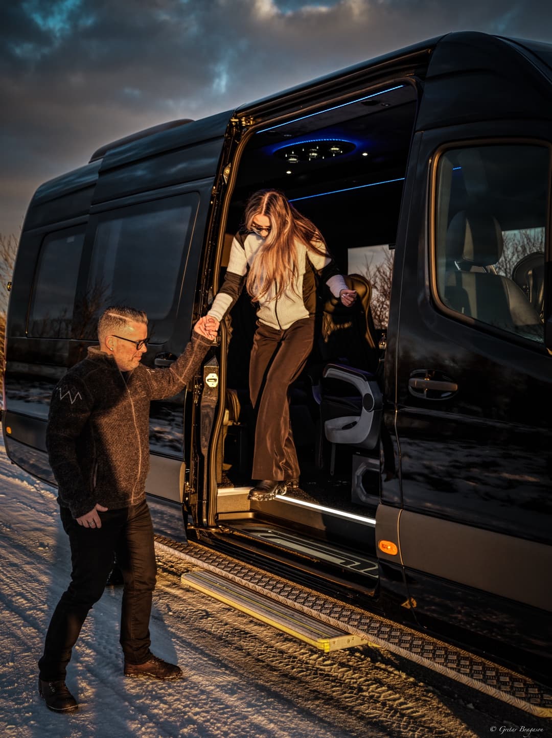 One Luxury chauffeur helping a guest step out of the Mercedes-Benz Sprinter at sunset
