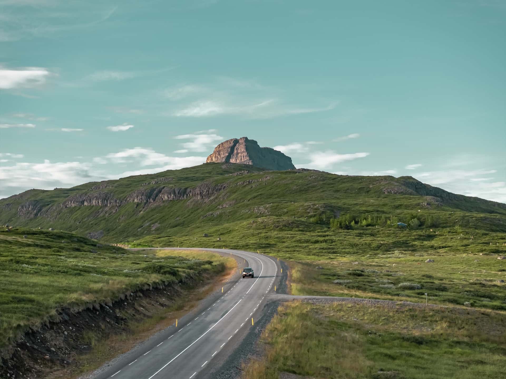 Land Cruiser on a winding road toward a rocky mountain peak in summer, Iceland