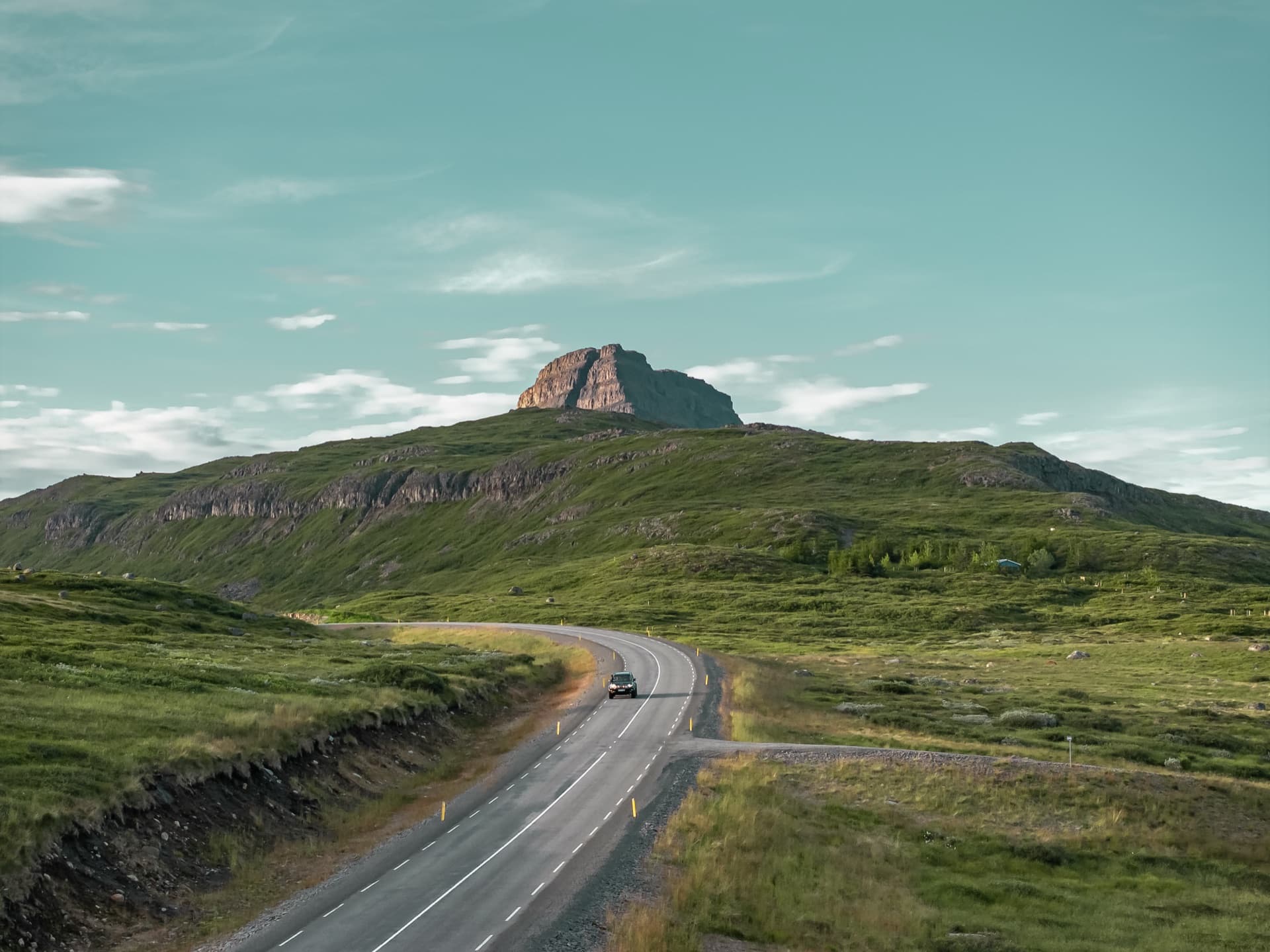 Land Cruiser on a winding road toward a rocky mountain peak in summer, Iceland