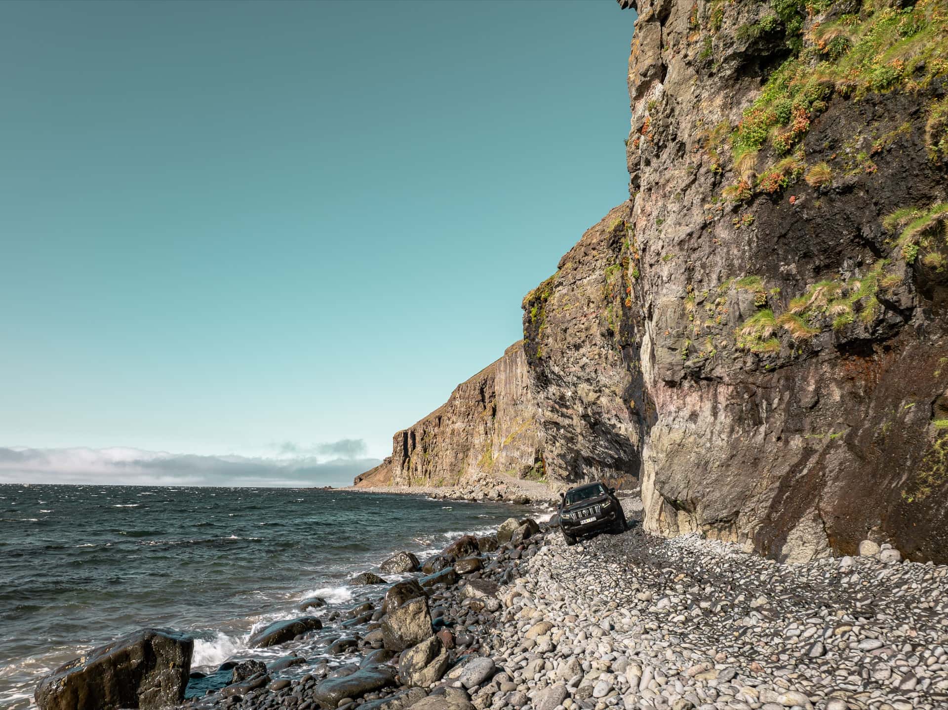 One Luxury Land Cruiser on the Svalvogavegur cliff road beneath sea cliffs in the Westfjords