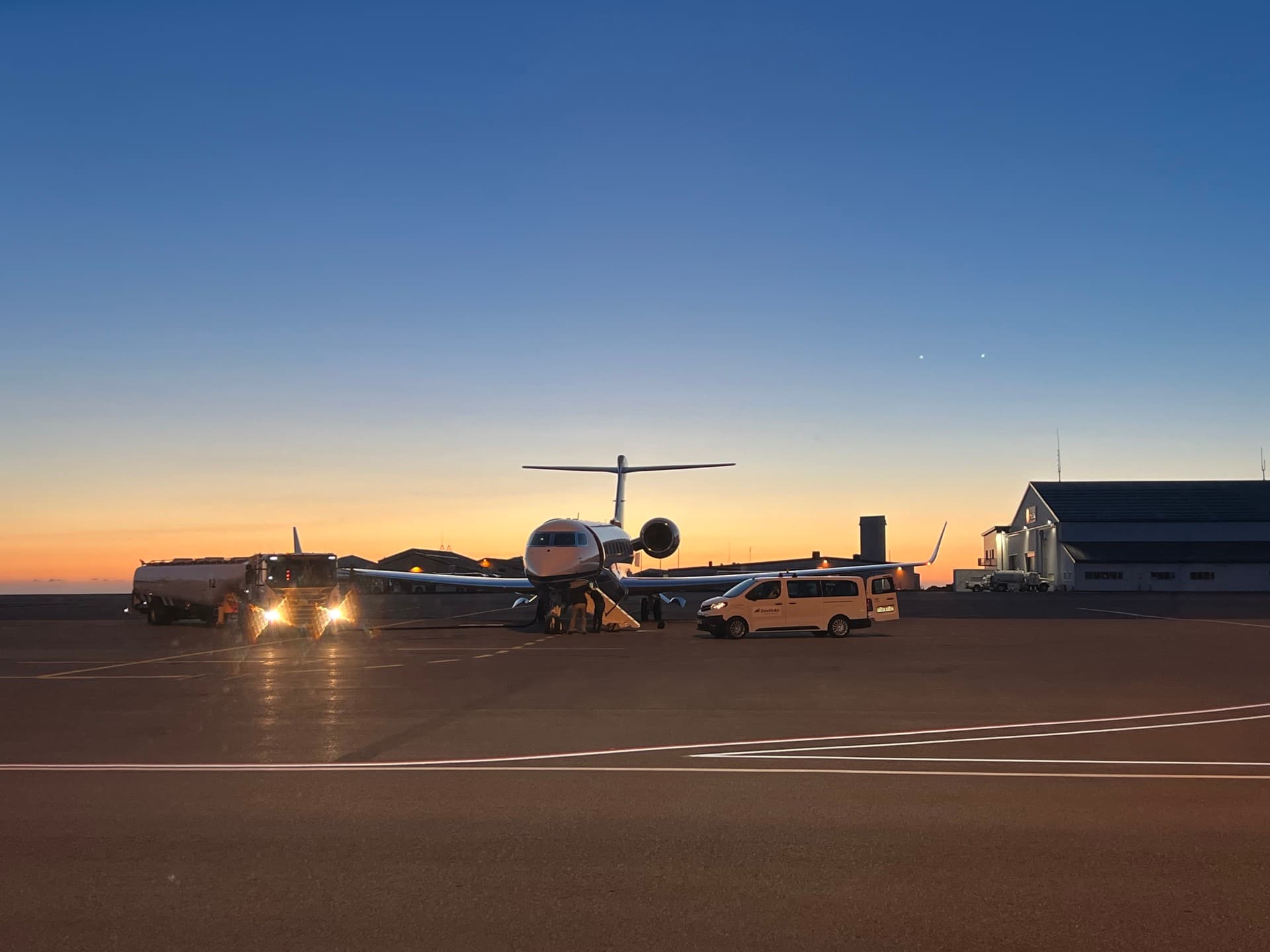 Private jet on the apron at Keflavík Airport at dusk with a One Luxury transfer vehicle waiting