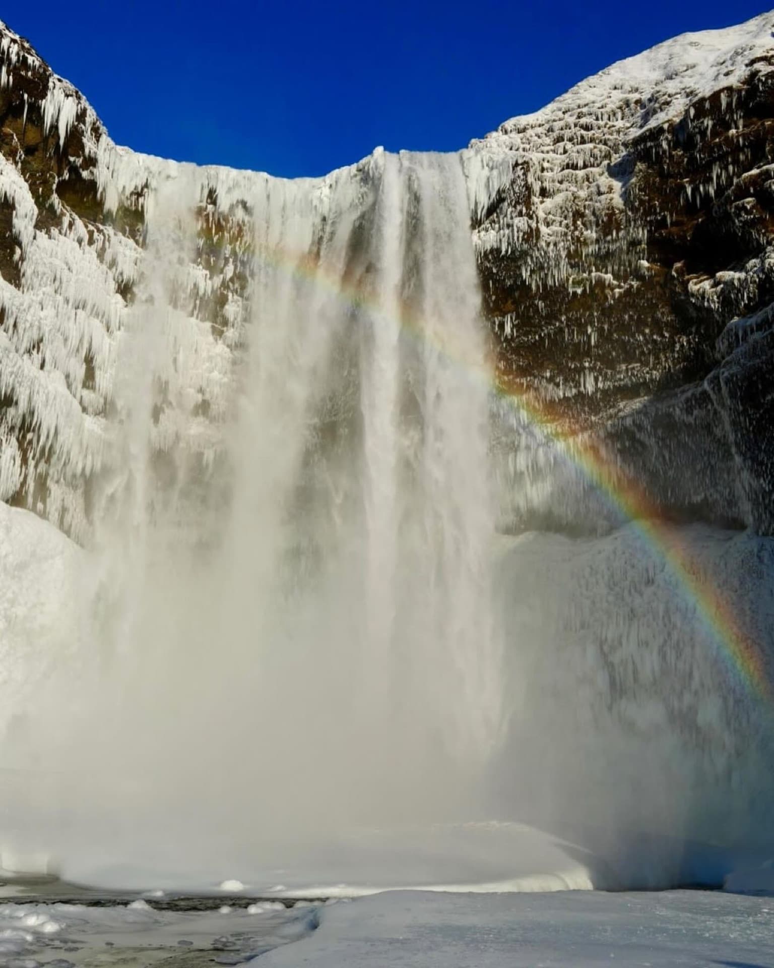 Skógafoss waterfall framed by ice and a rainbow in winter on Iceland's South Coast